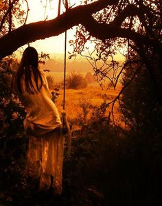 a woman is standing on a swing in the woods with her back to the camera