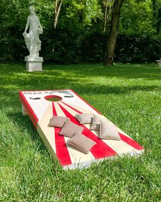 a giant cornhole game set up in the grass with a statue behind it and an american flag on top