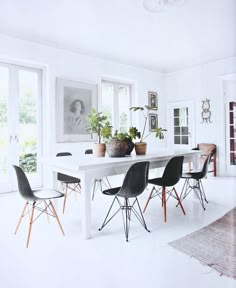 a white table with black chairs and potted plants on it in a dining room