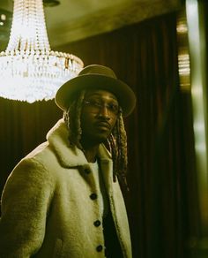 a man with dreadlocks and a hat standing in front of a chandelier