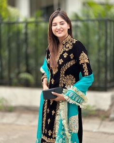 a woman standing in front of a fence wearing a black and blue outfit with gold details