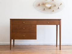 a wooden desk with two drawers and a clock on the wall in front of it