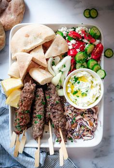 a tray with skewered meats, vegetables and pita bread on it