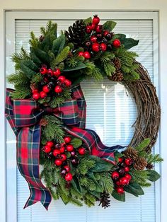 a christmas wreath with holly, berries and pine cones is hung on the front door