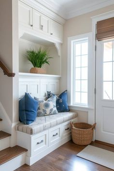 a window seat with blue pillows on it in front of a white wall and stairs