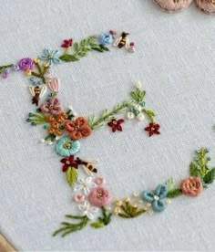 the letter e is made up of flowers and leaves on a white cloth with a wooden frame