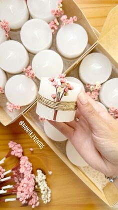 a person is holding a small box with candles in it and pink flowers on the side