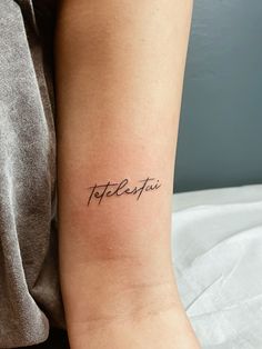 a woman with a tattoo on her arm that reads, totolosta in cursive writing