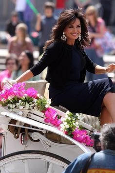 a woman in a black dress is riding on a horse drawn carriage with pink and white flowers