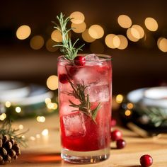 a drink with cranberry and rosemary garnish in a glass on a table