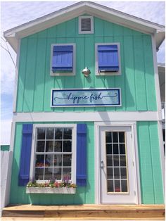 a green building with blue shutters on the front and windows that say happy fish