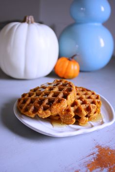 two waffles on a white plate next to pumpkins and blue vases