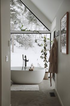 a white bath tub sitting inside of a bathroom next to a tall glass window covered in snow