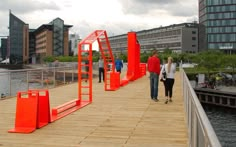 two people walking on a wooden bridge over water with buildings in the backgroud