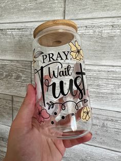 a hand holding a clear glass jar with the words pray, trust and flowers on it