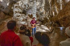 a group of people standing in a cave with a man playing an acoustic guitar while others watch