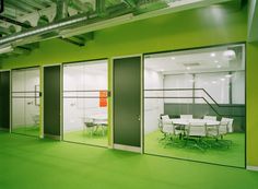 an office with green flooring and glass doors leading to the meeting room, which has white tables and chairs