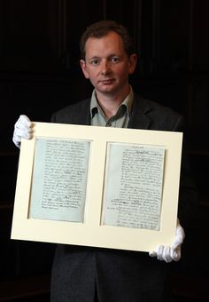 a man holding up two framed papers with writing on them in front of a dark background