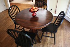 a wooden table with chairs around it and fruit on top of the table in front of them