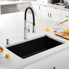 a kitchen sink with black faucet and bowl of lemons on the counter