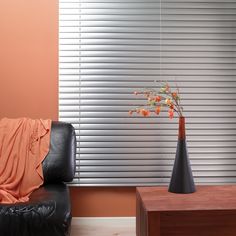 a black leather chair with an orange blanket on it in front of a window that has vertical blinds