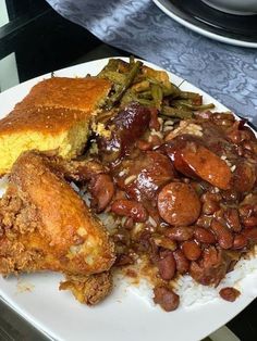 a white plate topped with meat, beans and cornbreads next to green beans