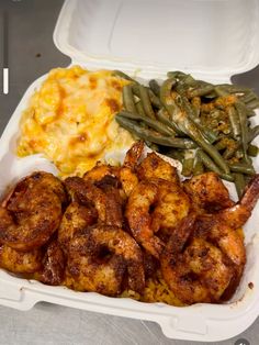 a plastic container filled with shrimp, green beans and mashed potatoes on a table