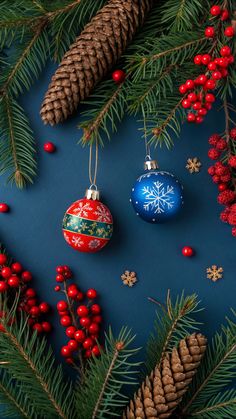 christmas ornaments and pine cones on a blue background with red berries, evergreen needles and fir cones