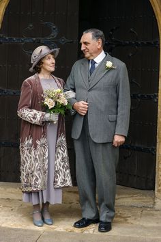 an older man and woman standing next to each other in front of a wooden door