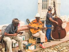 three men are playing instruments on the side of a building while another man sits down next to them