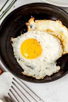 two fried eggs in a frying pan on top of a table with silverware