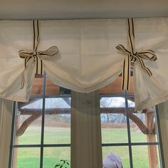 a window with two bow tie valances hanging from it's side and a cat sitting in the window sill