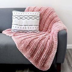 a gray couch with a pink blanket on it and a black and white throw pillow