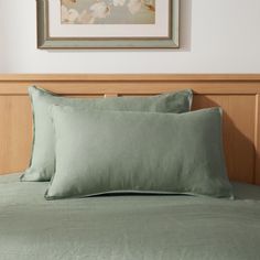 two light green pillows sitting on top of a bed next to a framed picture above it