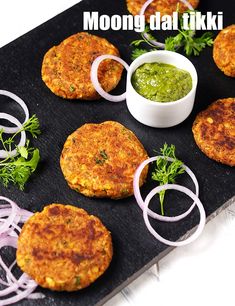 some food is on a black tray with onion rings and green sauce in the middle