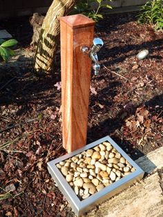 a wooden water fountain with rocks in the ground next to it and a tree behind it