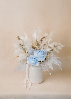 a white vase filled with blue flowers on top of a beige tableclothed surface