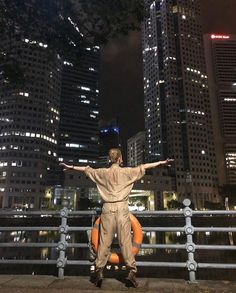 a man standing on the edge of a bridge in front of tall buildings at night