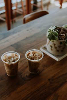 two cups of coffee sitting on top of a wooden table next to a potted plant