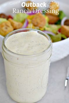 a bowl of salad with dressing next to it and a fork on the table in front