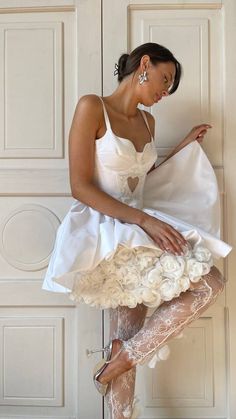 a woman in a white dress is leaning against a wall with her legs spread out