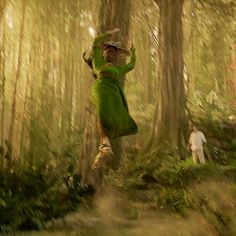 a woman in a green dress is running through the woods