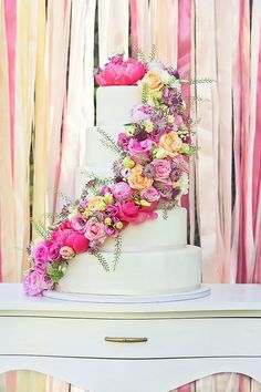 a wedding cake with pink and yellow flowers on the top is sitting on a table