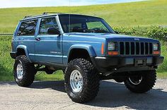 a blue jeep parked in front of a lush green field