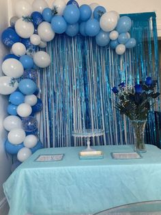 blue and white balloons are hanging over a table with a vase full of flowers on it