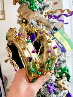 a person holding up a pair of gold shoes in front of a christmas tree with decorations