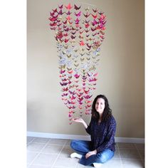 a woman sitting on the floor in front of a wall hanging with paper butterflies attached to it