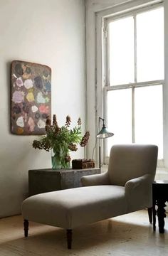 a white chair sitting in front of a window next to a vase filled with flowers