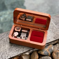 an open wooden box with several different types of watches inside on some rocks near the water