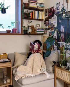 a person laying on a couch with a book in their hand and some plants behind them